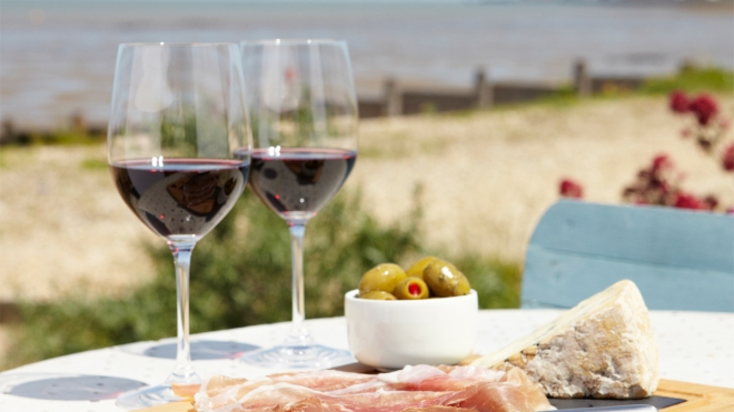 Two glasses of red wine on a table with the beach in the background